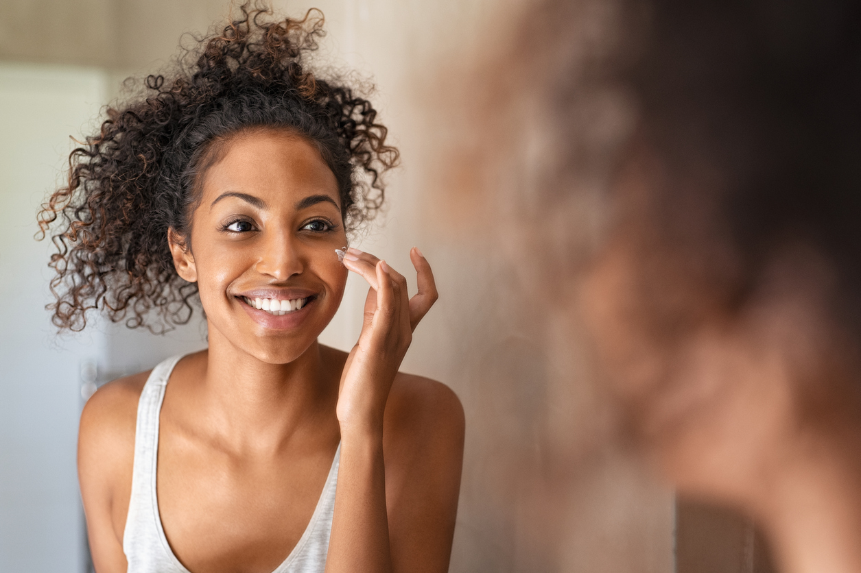 Woman applying sunscreen and moisturizer as part of a simple holiday skin care routine.