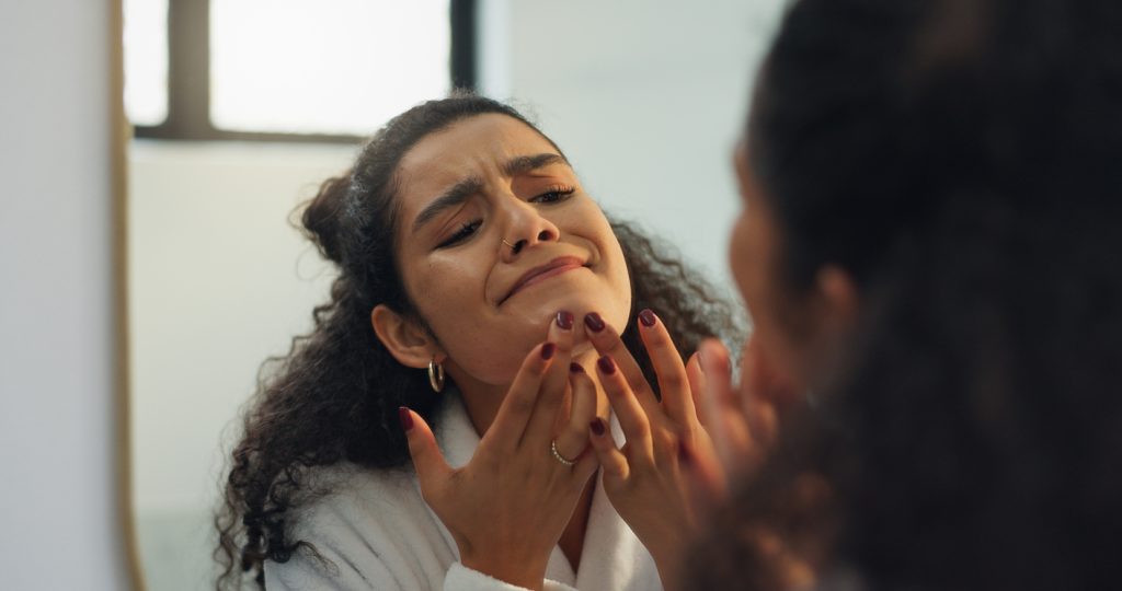 Woman in Tuscaloosa touching her chin while noticing holiday stress breakouts in the mirror.