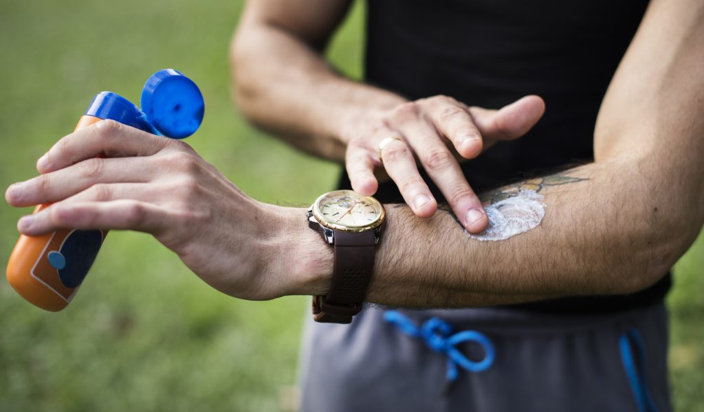 Person applying SPF sunscreen to a healing forearm tattoo removal site outdoors in summer heat.