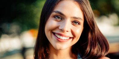 Young woman with glowing skin smiling outdoors in summer, representing pre-event skin treatments at a Tuscaloosa medspa.