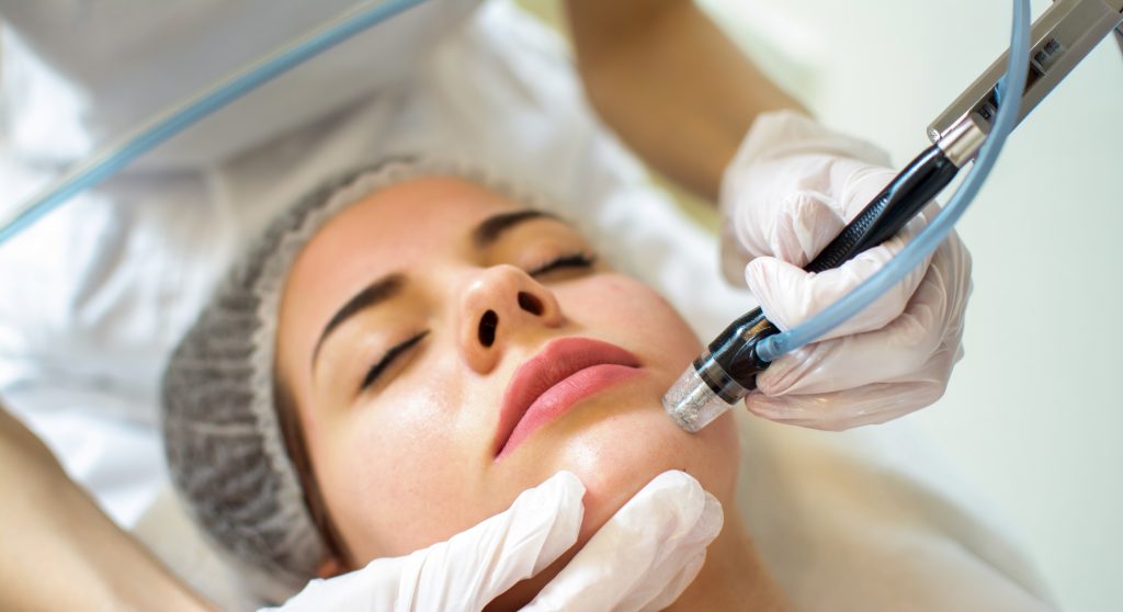 Esthetician performing a HydraFacial treatment on a woman's face at Tuscaloosa MedSpa before a campus event.